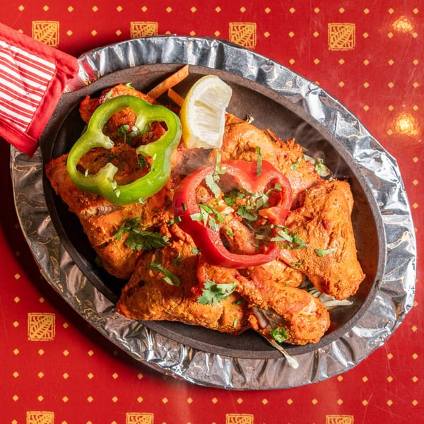 Sizzling tandoori chicken with bell peppers, cilantro, and lemon on a hot platter.