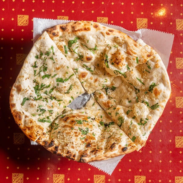 Garlic naan bread, cut into pieces, topped with cilantro and garlic, on a red patterned tablecloth.