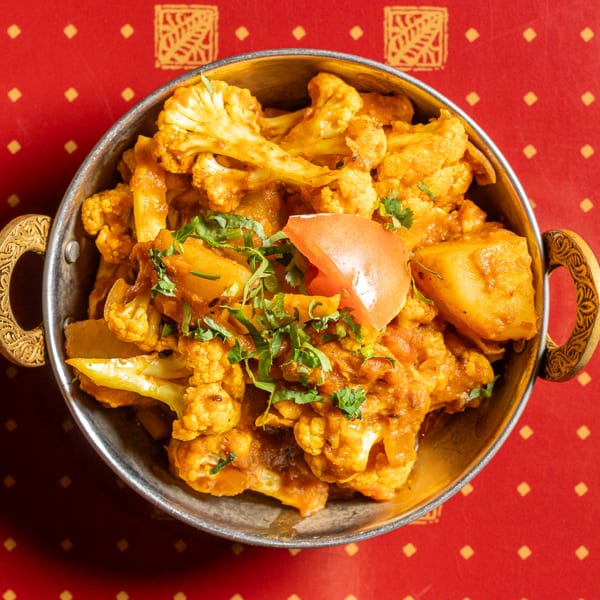 Aloo Gobi, an Indian dish with cauliflower and potatoes, garnished with cilantro and a tomato slice.