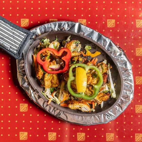 Sizzling chicken fajitas with bell peppers and lemon in a cast iron pan on a red tablecloth.