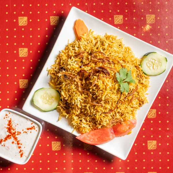Golden biryani rice with fried onions, cilantro, cucumber, tomato, and a side of raita.